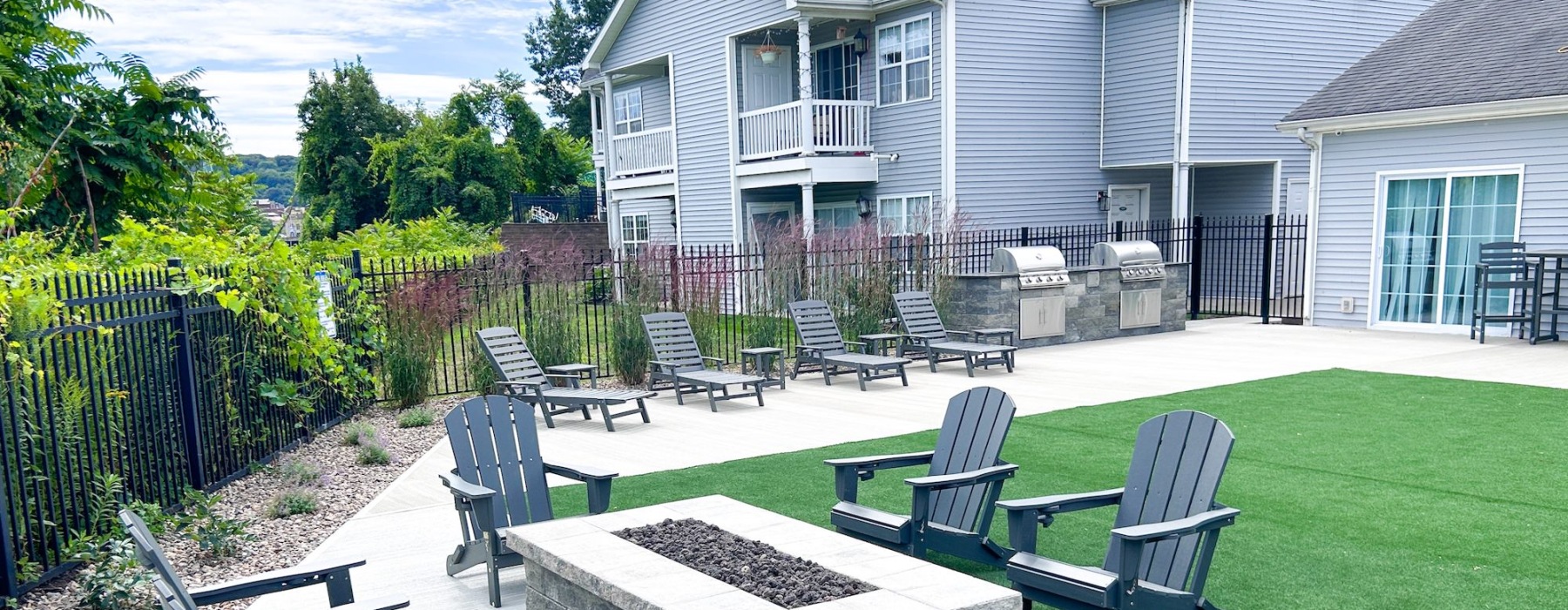 chairs around a fire pit with turf and a building behind it